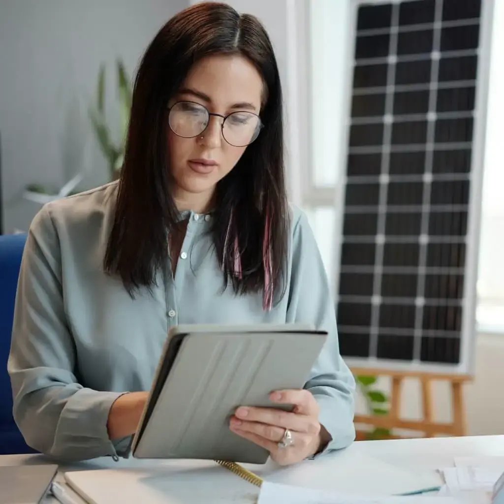 An office clerk holding a tablet with a solar panel in the background