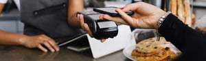 Customer making a contactless payment with a phone at a bakery counter