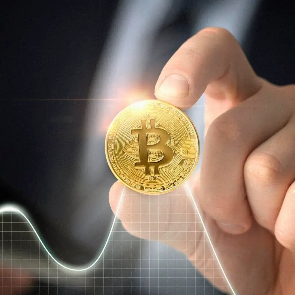 Hand holding a Bitcoin coin with a glowing effect and graph overlay